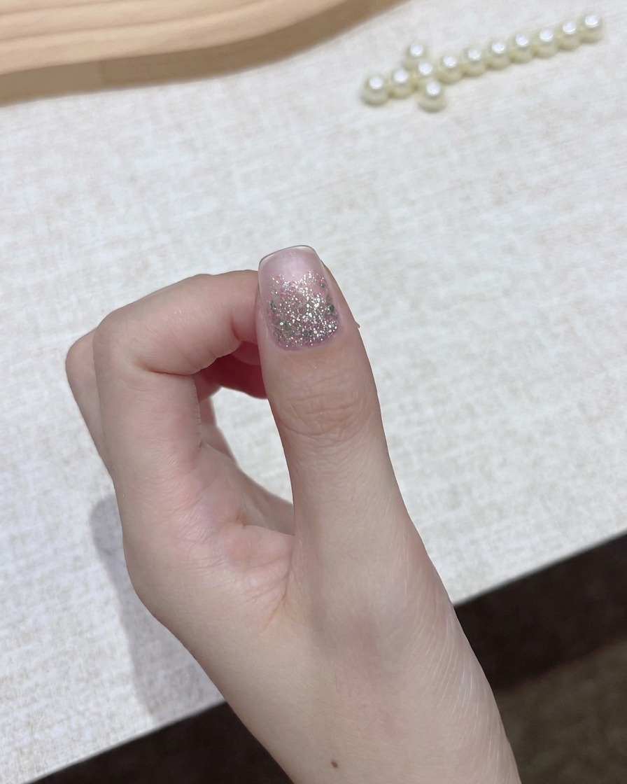 Una mano sosteniendo un frasco de esmalte de gel oscuro con la tapa retirada, preparándose para el paso de aplicación.