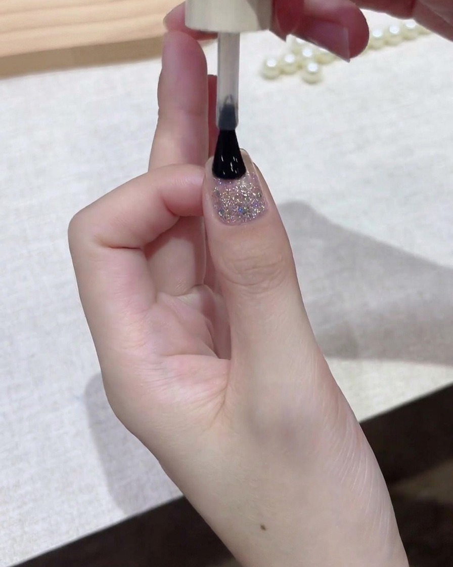 Un pincel de esmalte aplicando una capa fina de gel oscuro sobre la superficie de la uña.