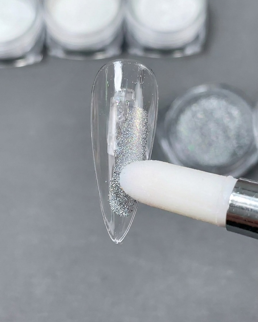 Un aplicador de esponja colocando polvo láser holográfico plateado sobre una punta de uña stiletto transparente.