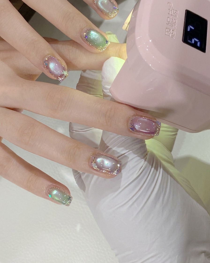 Una toma de cerca de la mano de una clienta posicionada bajo una mini lámpara de uñas UV/LED rosa para el curado.