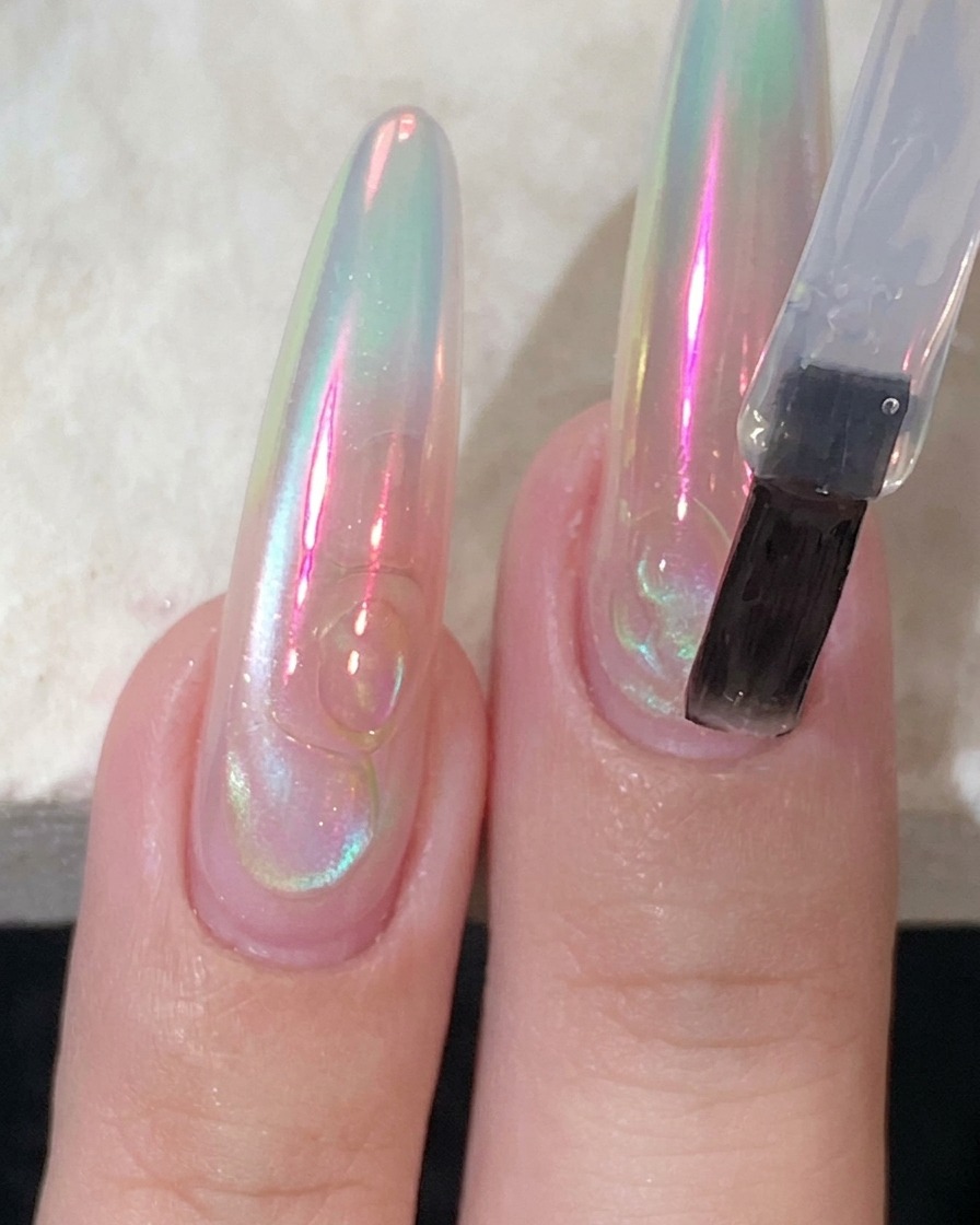 Un pincel plano aplicando un top coat transparente y brillante sobre una uña larga.