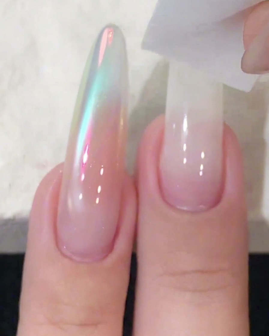 Un bloque de esponja dando toques y difuminando esmalte de gel blanco sobre una uña larga.