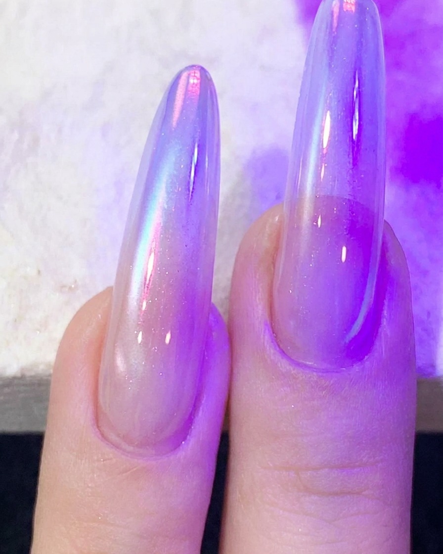 Dedos con gel de uñas ojo de gato curándose bajo una lámpara UV/LED morada.