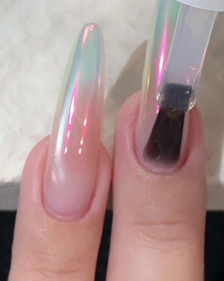 Un aplicador de esponja frotando polvo cromado sobre una uña brillante hasta que refleja un brillo aurora.