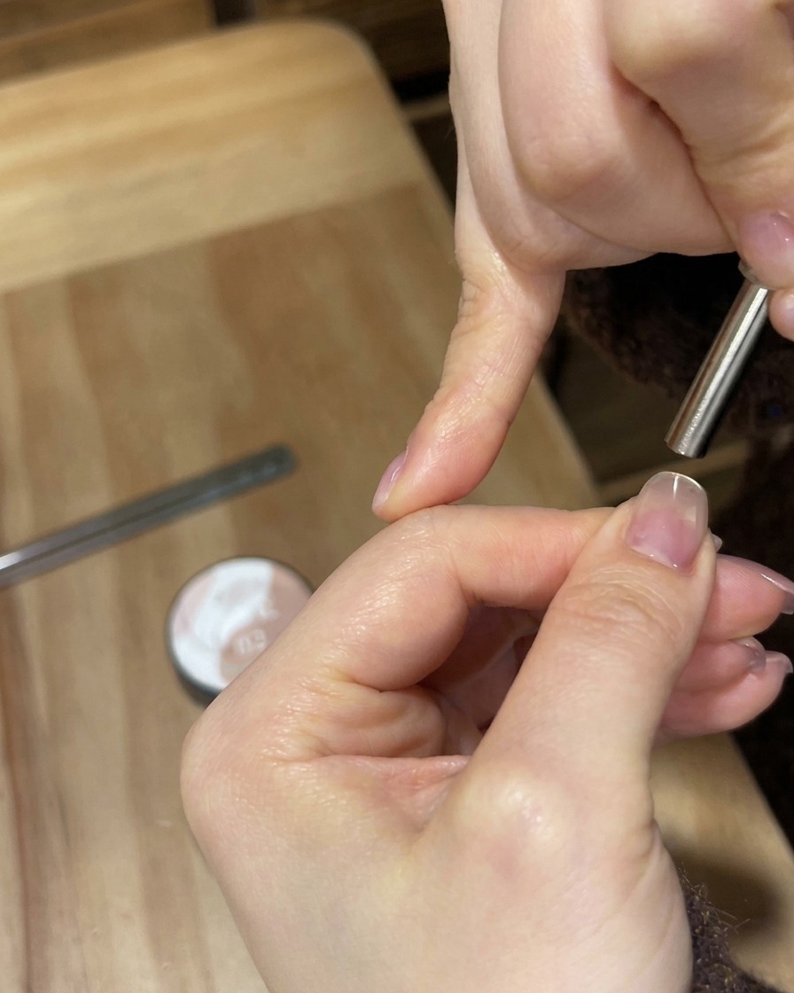 Una lámpara UV/LED blanca portátil brillando con luz brillante sobre una uña para curar la capa de gel.