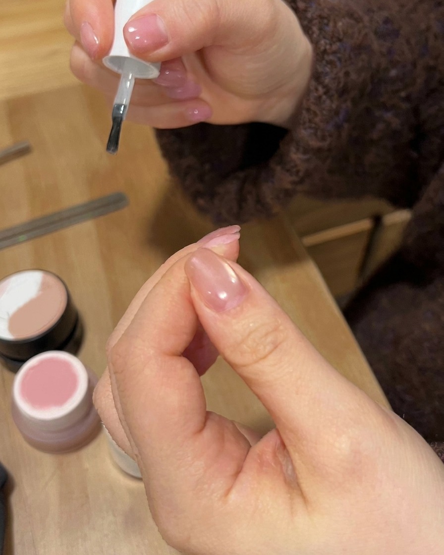 Un pincel de esmalte de uñas aplicando una capa transparente brillante sobre un diseño de uña con degradado terminado.