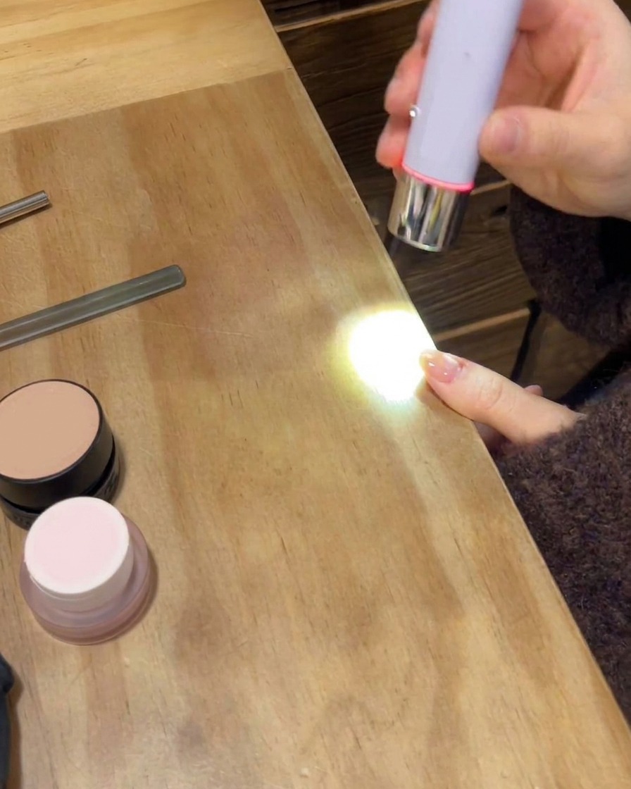 Una lámpara UV/LED portátil curando la capa superior brillante final en una mano con manicura.