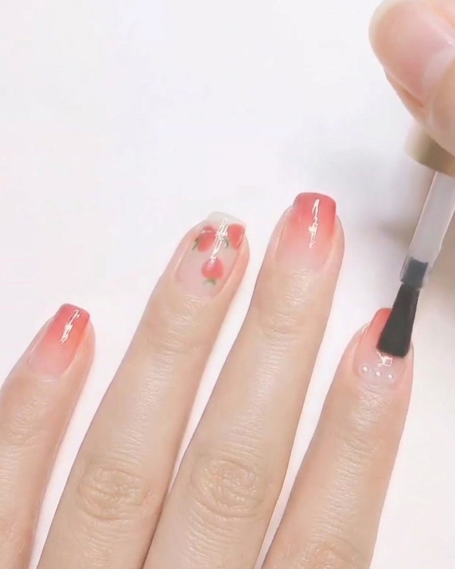 Un pincel de uñas aplicando una capa superior transparente sobre un diseño de uñas terminado que presenta pequeñas perlas encapsuladas.