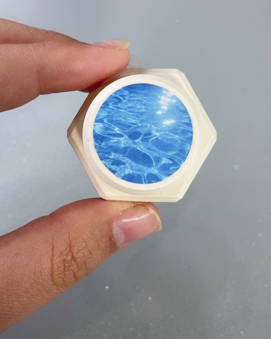 Un primer plano de un pincel de uñas aplicando un gel de vidrio azul transparente en la punta de la uña.