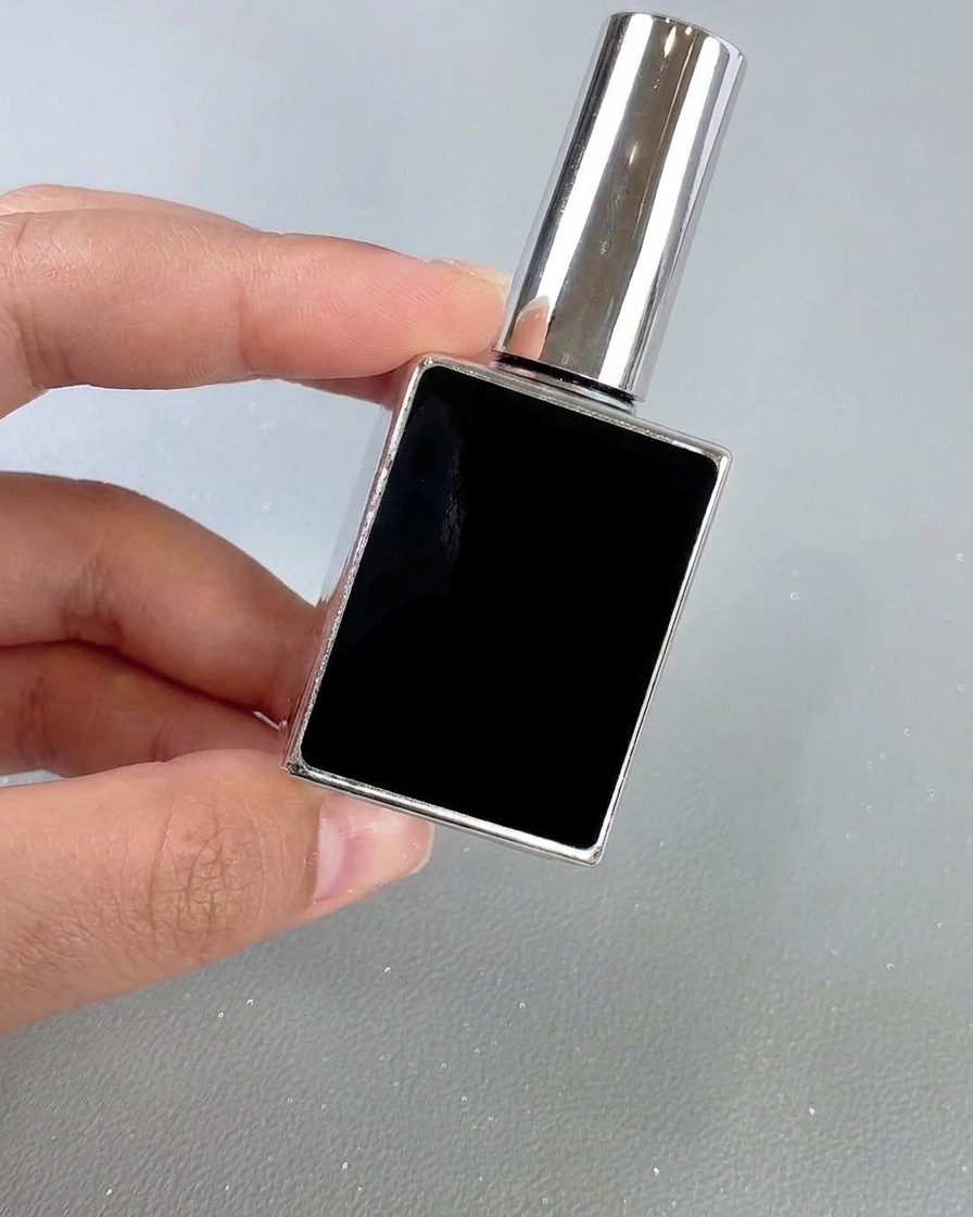 Un frasco cuadrado negro y plateado de top coat de uñas sostenido con la mano frente a un fondo neutro.
