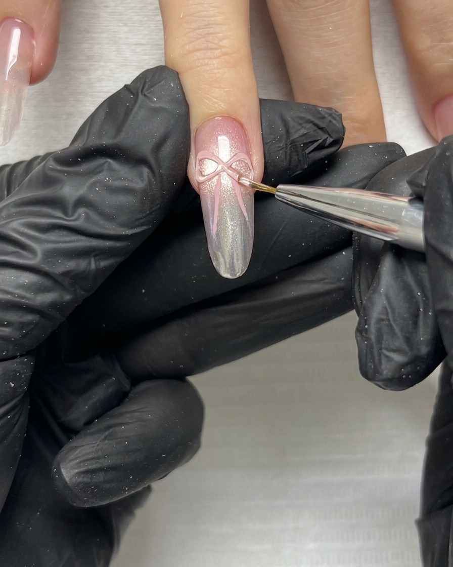 Una toma en primer plano de un pincel fino refinando los bordes delicados y las colas de un lazo de cinta rosa 3D en una uña manicurada.