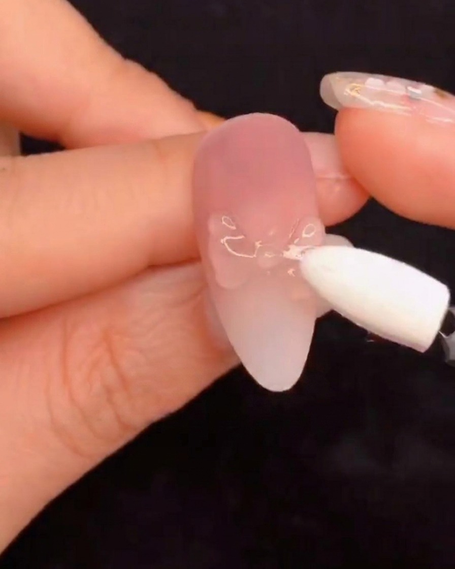 Un aplicador de esponja de silicona frotando polvo de pigmento aurora sobre un diseño de uña esculpida.