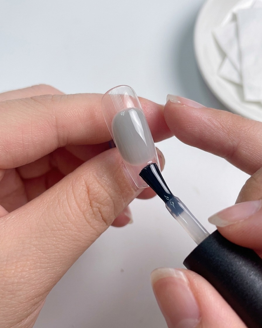 Un pincel aplicando una capa de top coat sobre una uña maquillada.