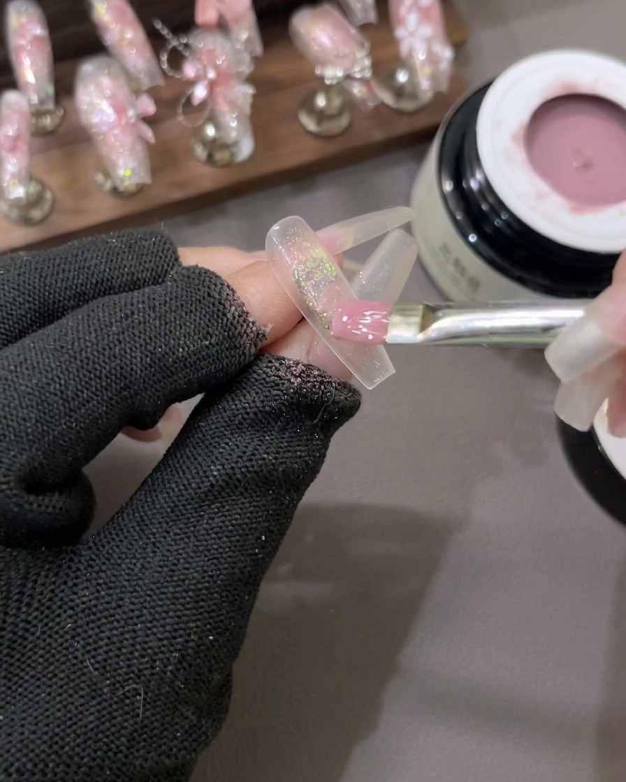 Un pincel plano de gel esparciendo un esmalte de gel rosa lechoso semitransparente sobre una uña con escamas de purpurina en el centro.