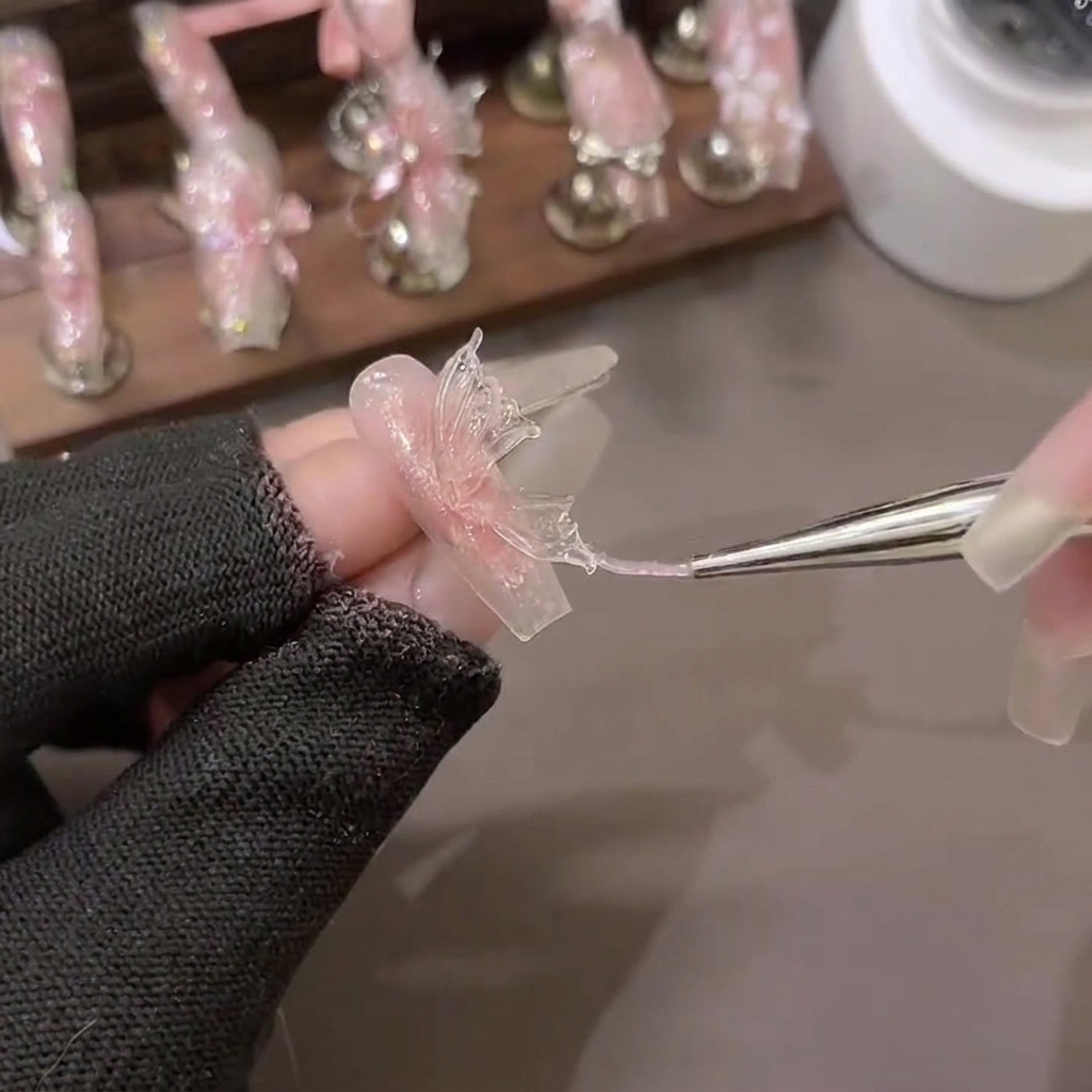 Un pincel de tallado dando forma a un triángulo de gel de extensión suave de PVC en alas de mariposa detalladas sobre papel de respaldo.