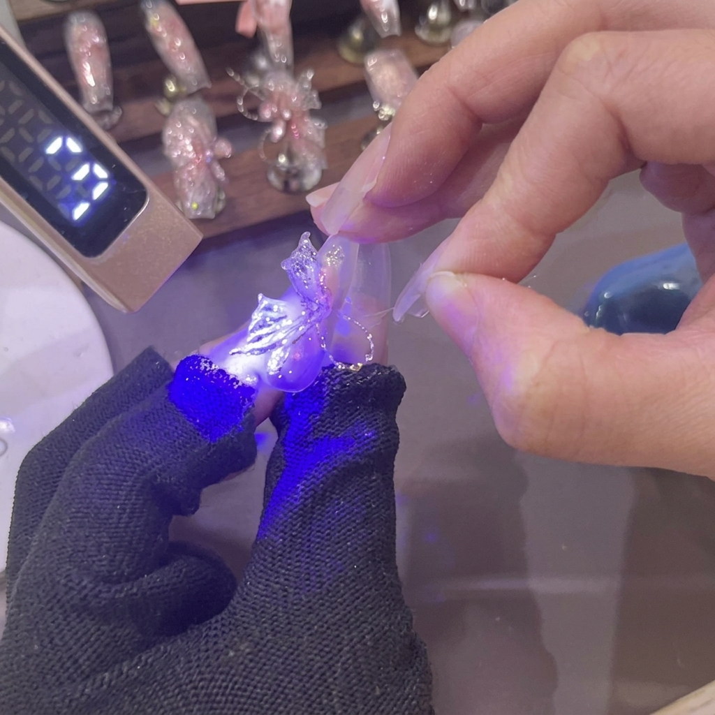 Una mini lámpara UV brillando con luz púrpura sobre un ala de mariposa de gel rosa 3D recién formada en la uña.