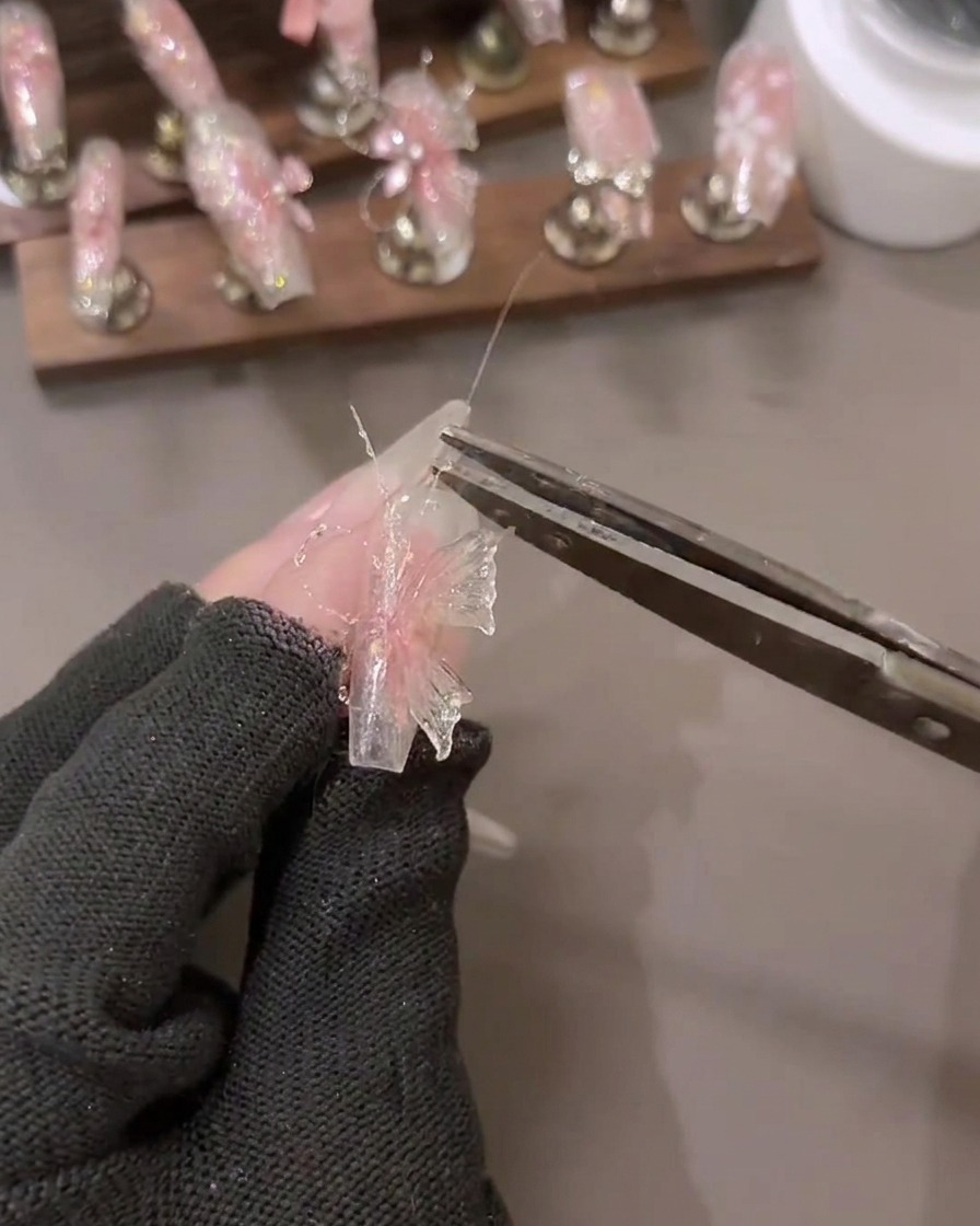 Un primer plano de una mano aplicando detalles de gel de purpurina de diamante triturado en un diseño de arte de uñas 3D con herramientas cercanas.