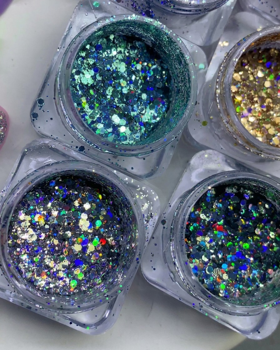 Vista cenital de varios tarros pequeños llenos de escamas de purpurina colorida, holográfica y metálica.