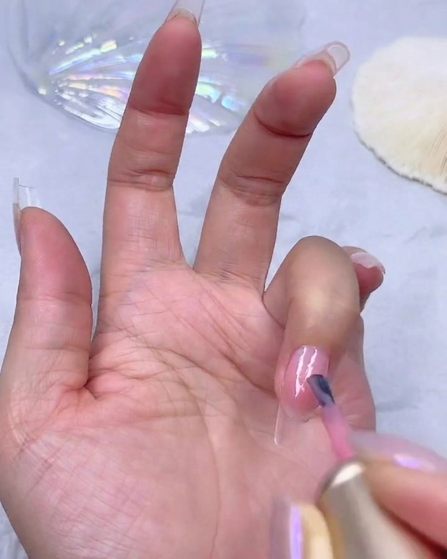 Aplicando una segunda capa de esmalte en gel rosa translúcido para aumentar la opacidad del color en la uña.