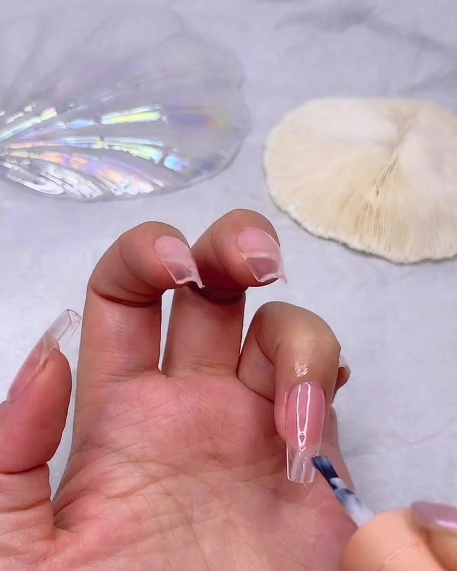 Un pincel aplicando una capa de esmalte en gel blanco lechoso en la punta de una uña de tono rosa para iniciar el efecto ombré.