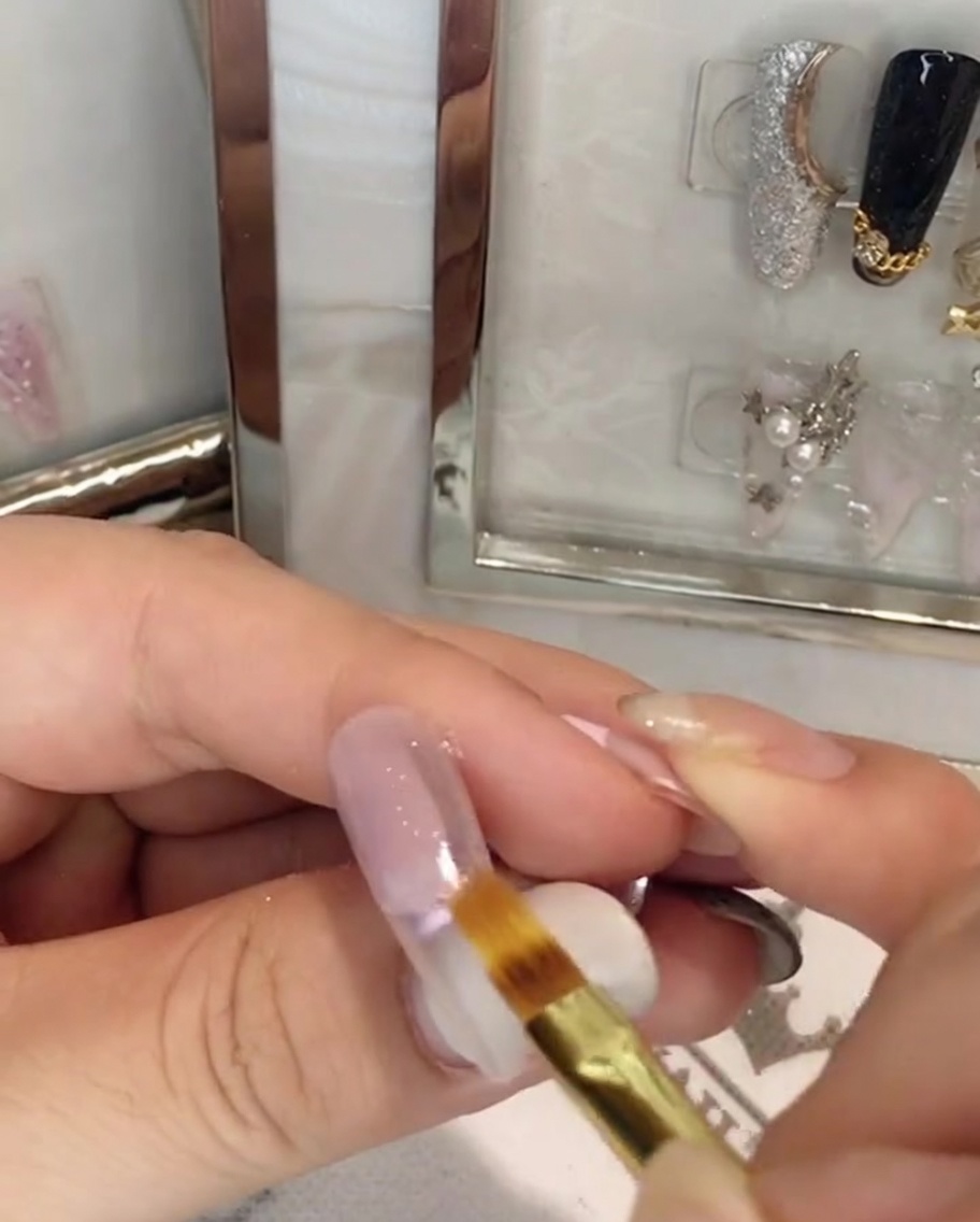 Un pincel plano de uñas difuminando el gel rosa hacia abajo en el centro de la placa ungueal.