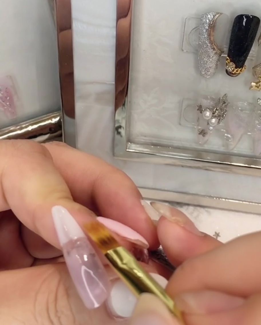 Un pincel plano difuminando el esmalte en gel blanco hacia arriba dentro del gel rosa en la uña.