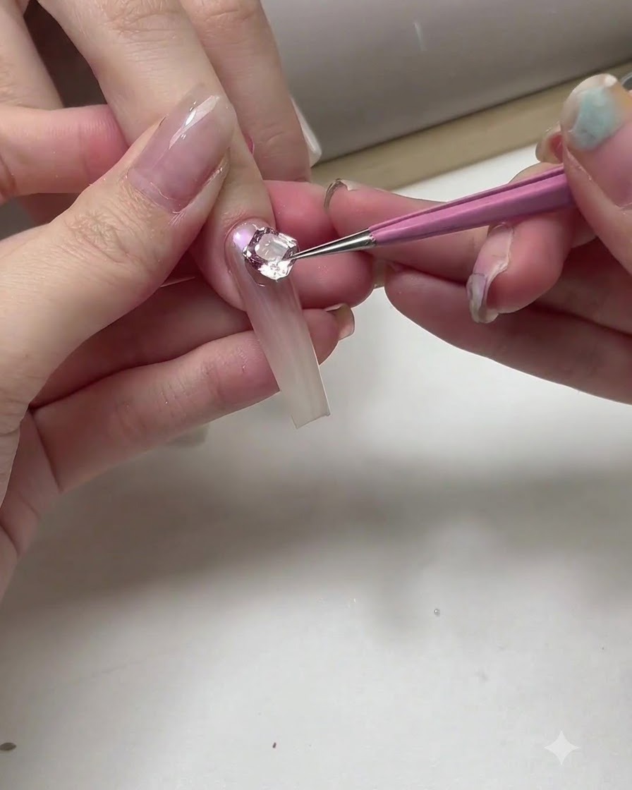 Primer plano de un manicurista usando un pincel fino y gel plateado para añadir contornos curvos delicados cerca de un gran cristal en una uña.