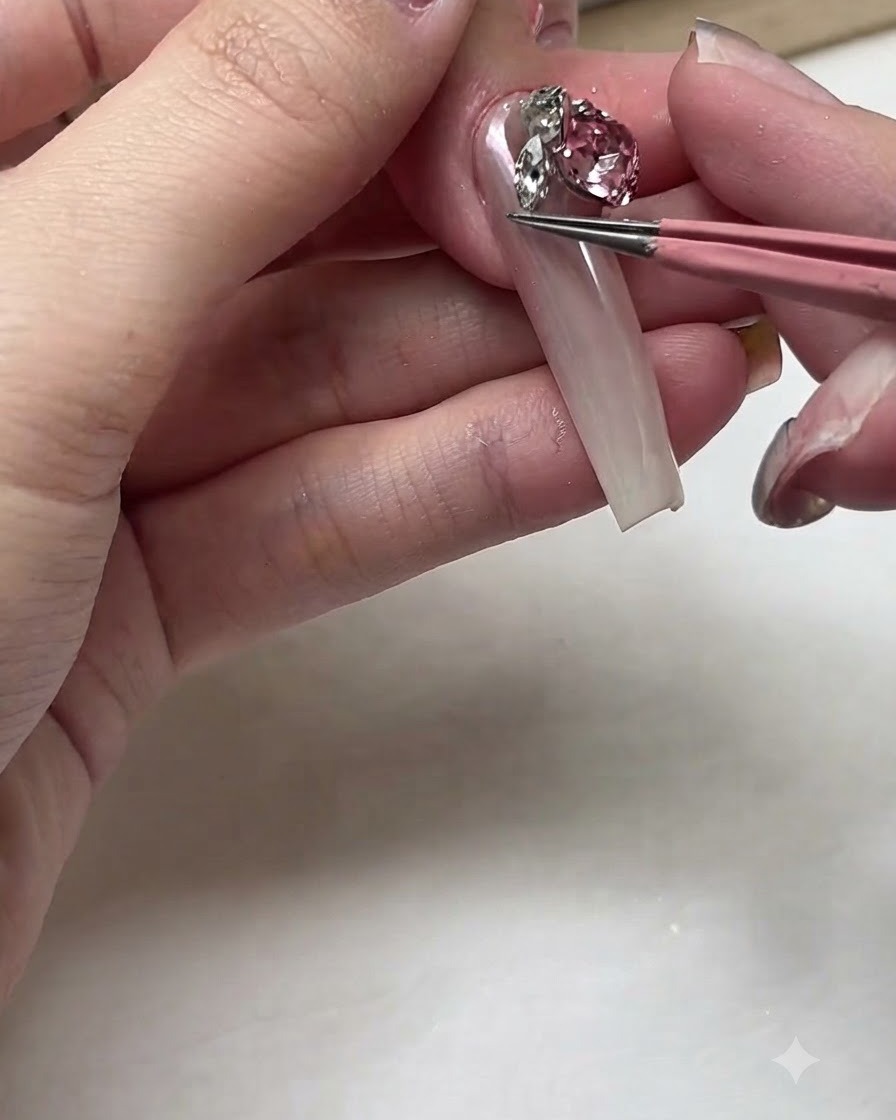 Pinzas colocando un cristal rosa grande y brillante cerca de la cutícula de una uña larga.