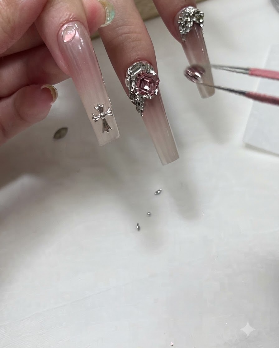 Manicurista usando pinzas para colocar un pequeño dije de cristal cerca de la base de una uña ombré larga.