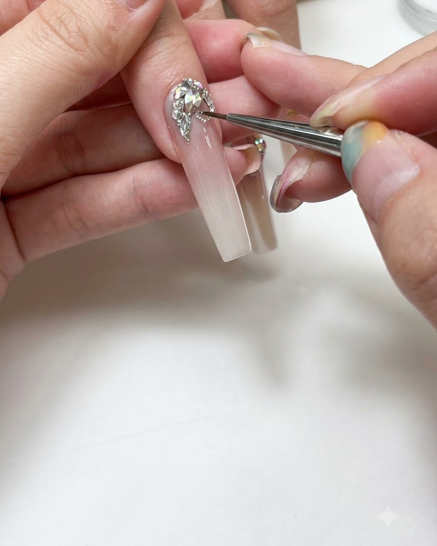 Primer plano de un manicurista utilizando un pincel fino para pintar líneas de gel plateadas alrededor de cristales.