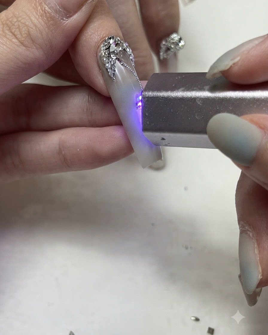 Linterna UV/LED portátil curando finas líneas de gel plateadas y pedrería en una uña.