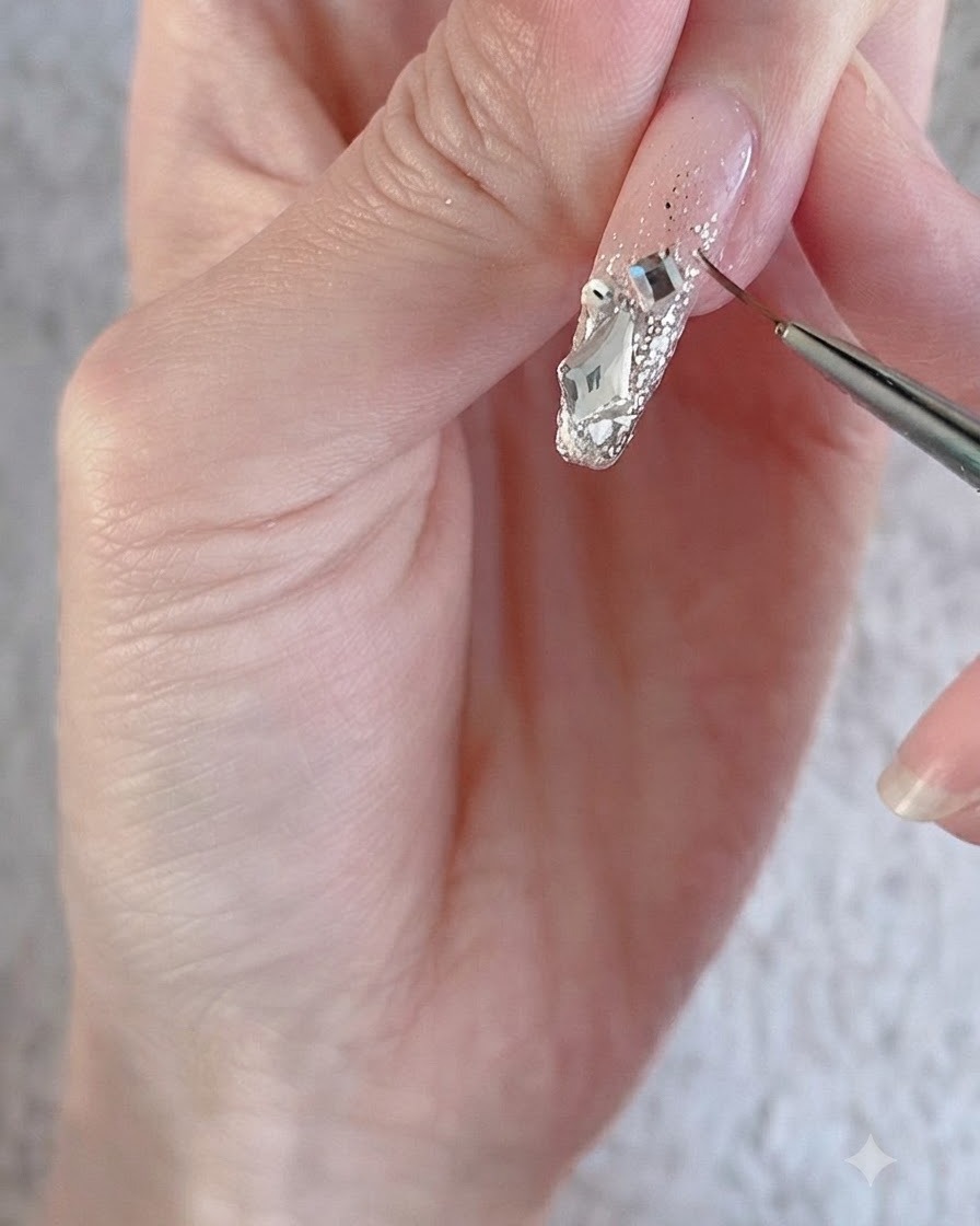 Un pincel delineador fino perfilando grandes cristales brillantes y dijes sobre la superficie de una uña decorada.