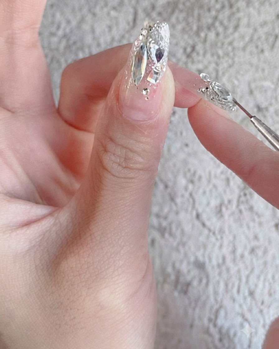 Un pincel de uñas aplicando un top coat de refuerzo brillante sobre un diseño de uña con pedrería totalmente finalizado.