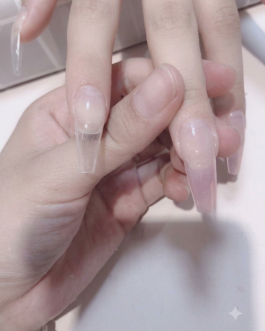 Un pincel de uñas difuminando el gel rosa translúcido hacia abajo sobre una extensión de uña translúcida para formar un efecto degradado.