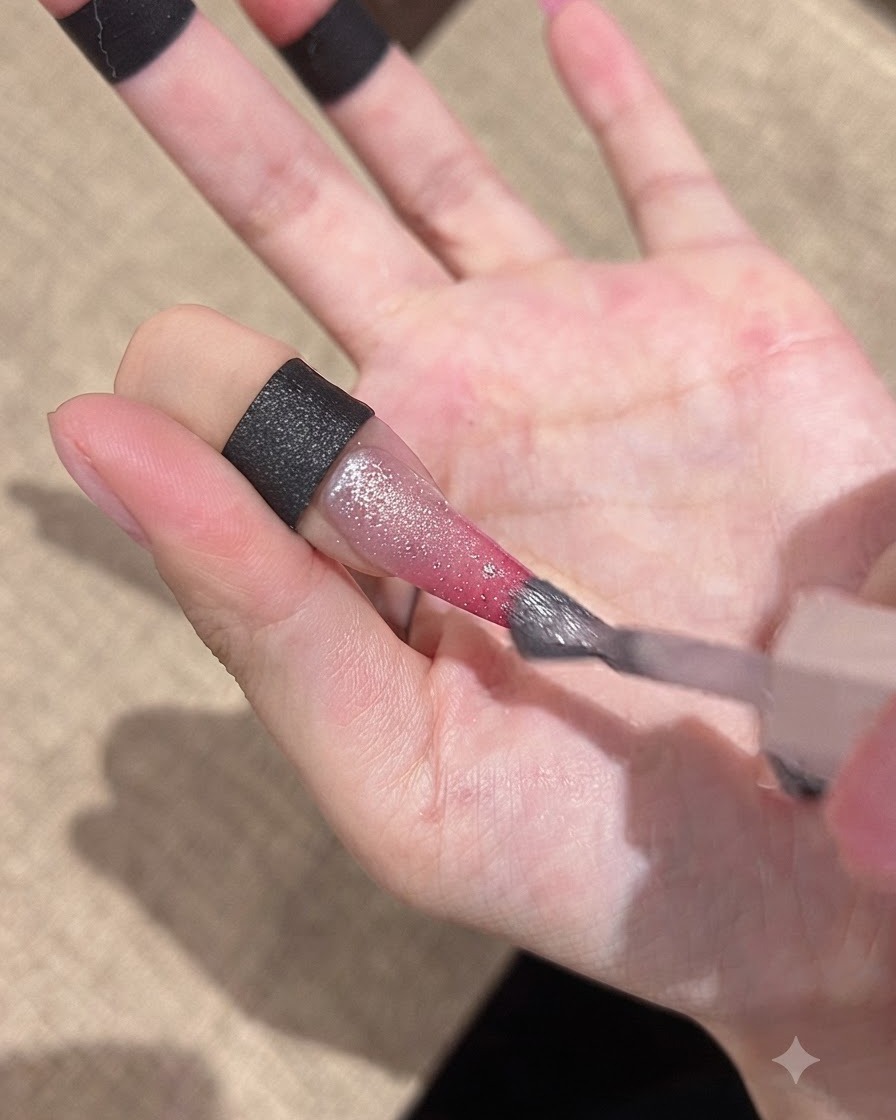 Un pincel aplicando un gel cat-eye brillante sobre la superficie de la uña degradada.