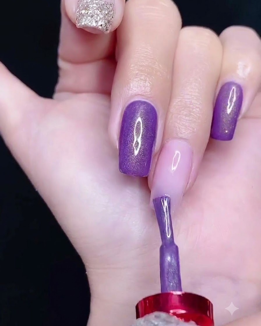 Un pincel aplicando esmalte de gel morado en la parte superior de la uña.