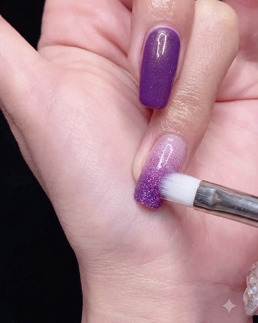 Un pincel para degradados difuminando el esmalte de gel morado hacia abajo para lograr un efecto ombré suave.