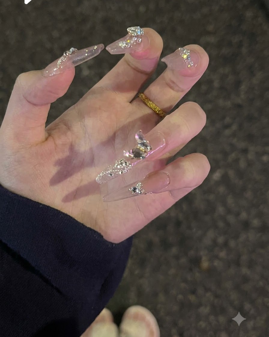 Mano girada hacia arriba para mostrar la purpurina en la superficie y los brillantes cristales tipo diamante sobre las uñas nude.