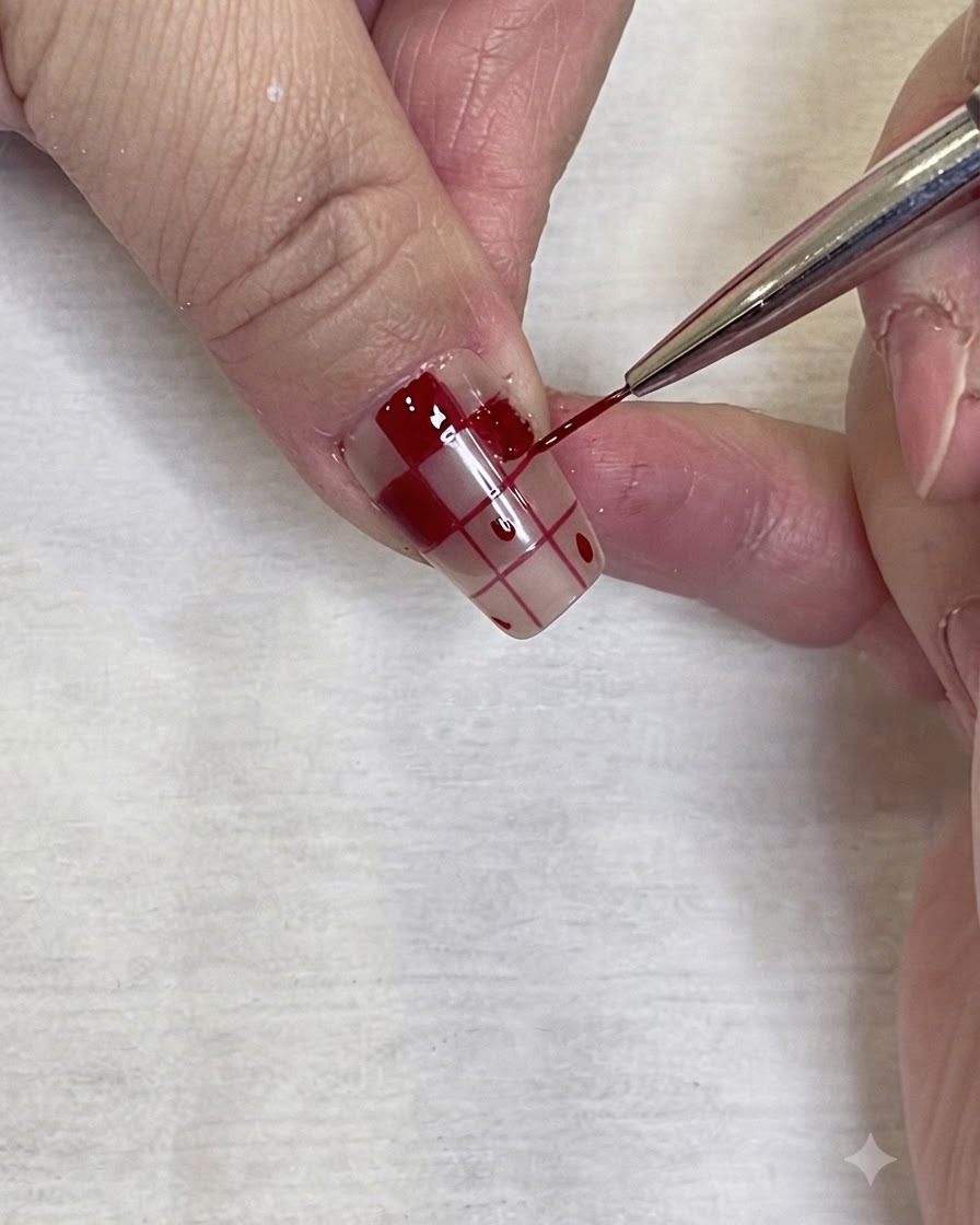 Un primer plano detallado de un pincel fino de arte de uñas aplicando con precisión esmalte en gel rojo en el borde de un patrón de cuadros en una uña.