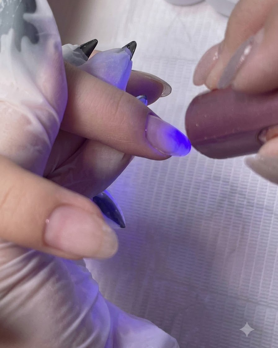 Una mini lámpara portátil UV/LED curando la capa base en el dedo de un cliente.