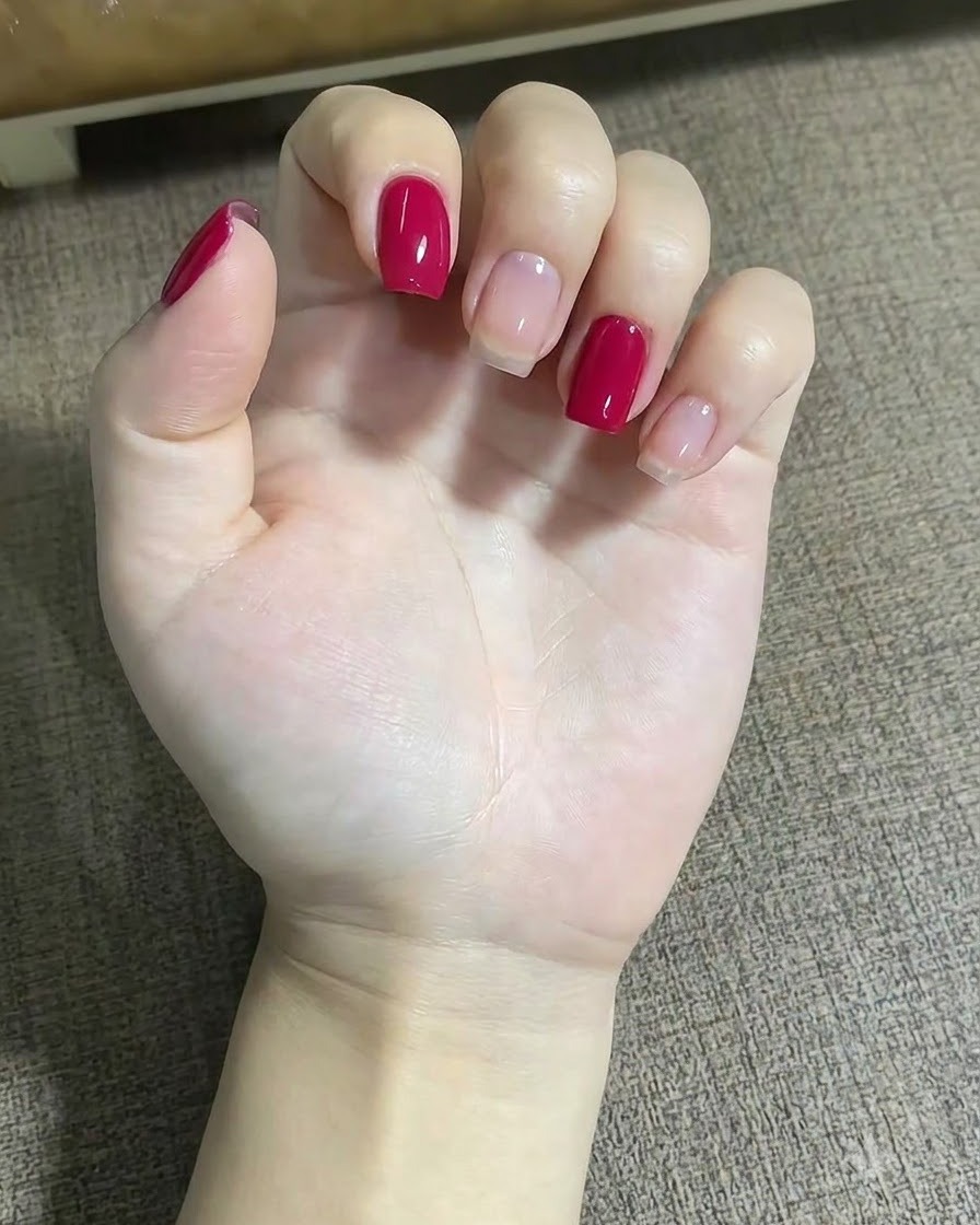 Un primer plano de una mano utilizando un pincel delineador fino para aplicar pequeños puntos rojos cerca de un diseño de estrella en el dedo medio.