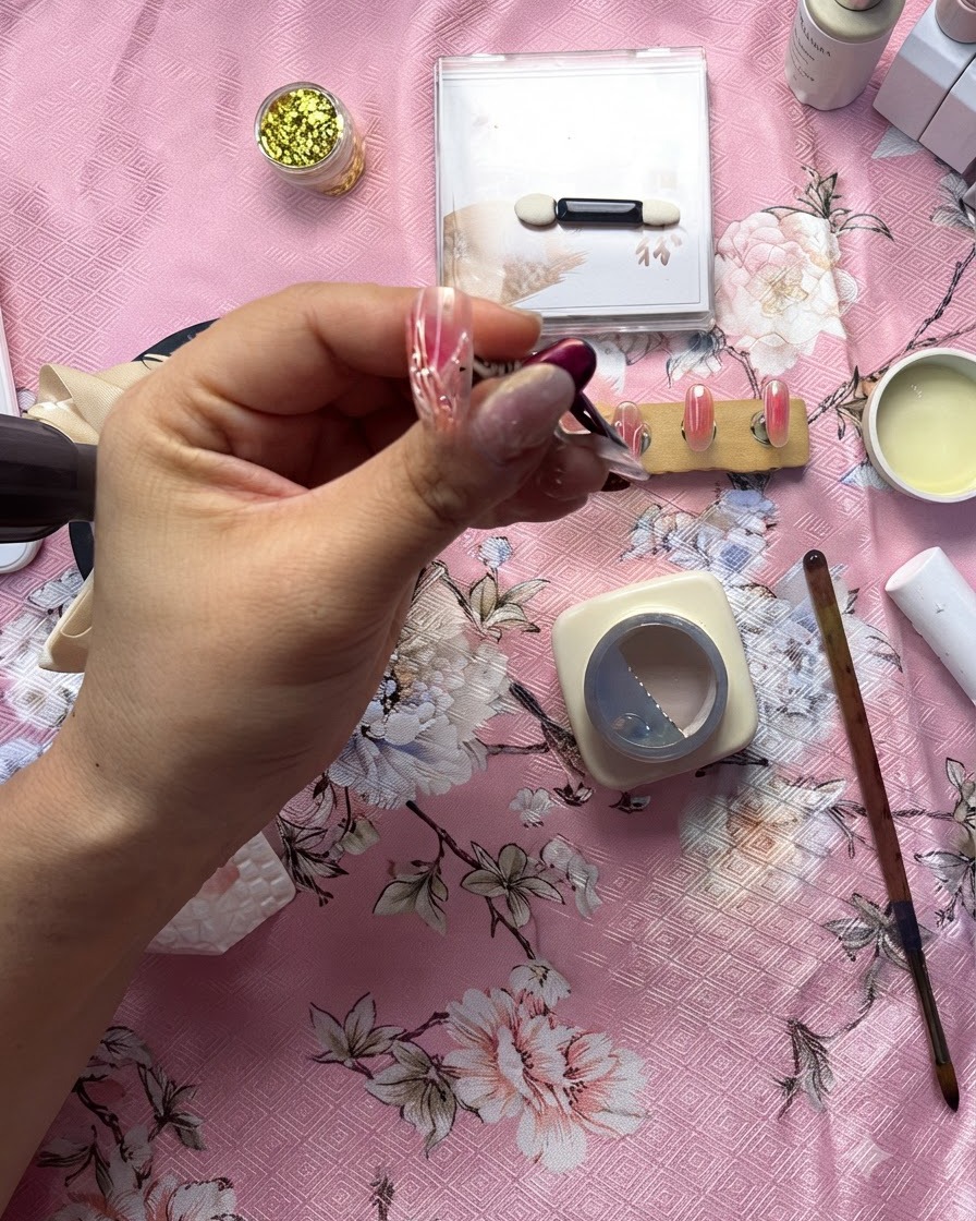 Un primer plano detallado de una manicurista usando un pincel fino para aplicar una línea de gel transparente en relieve sobre un diseño de corazón blanco.