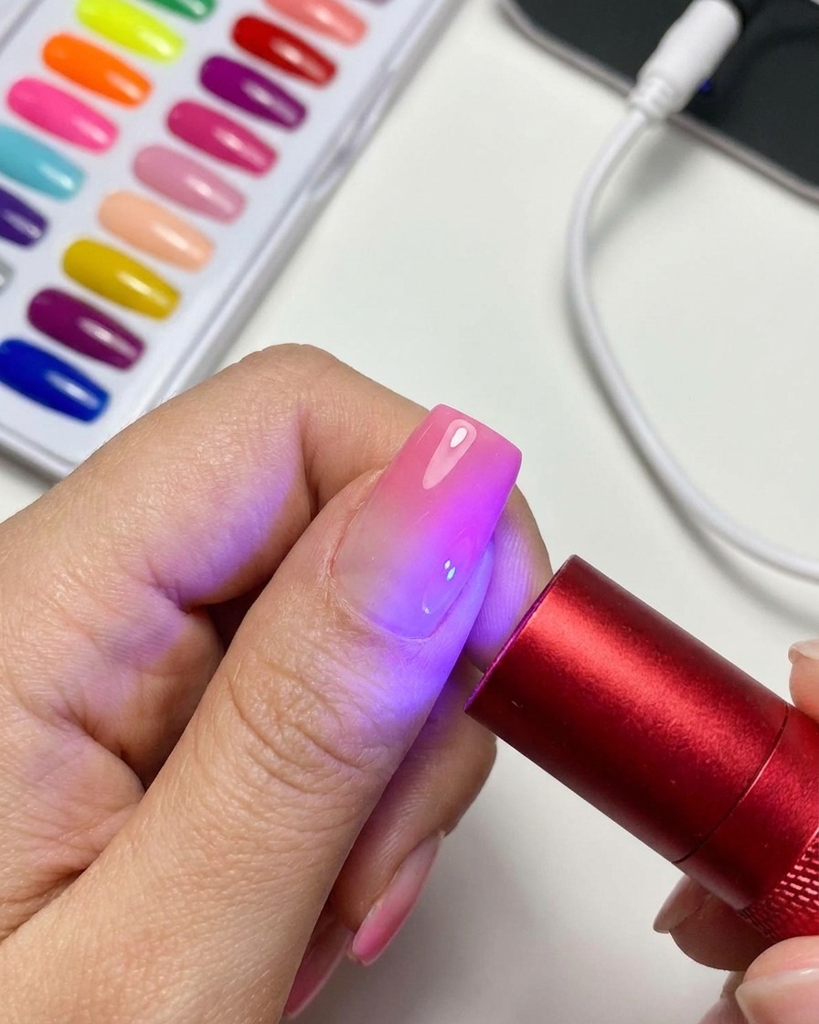 Una lámpara UV/LED roja portátil iluminando una uña de gel magnética de ojo de gato terminada.