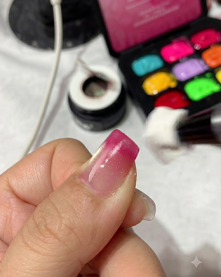 Una esponja aplicadora aplicando esmalte de gel rojo magenta en la punta de un dedo para construir un degradado.