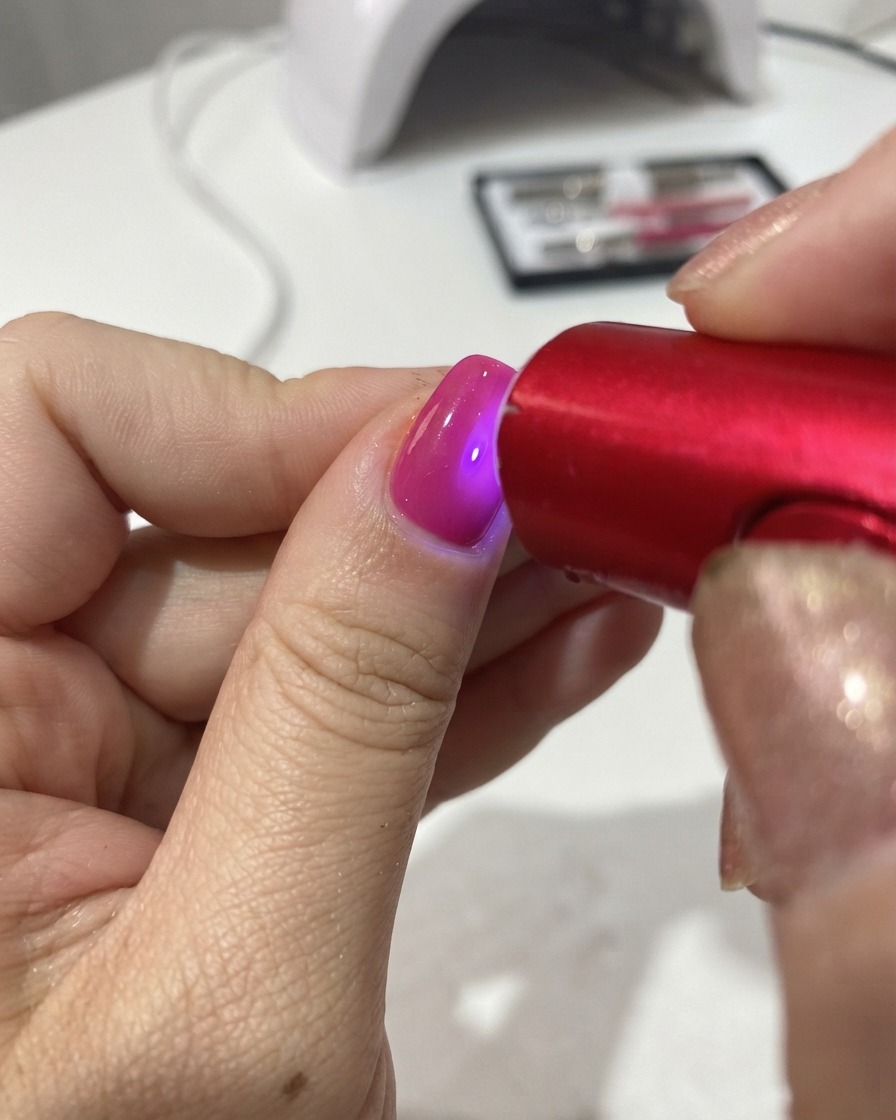 Una lámpara UV/LED roja portátil curando el esmalte de gel en una uña.