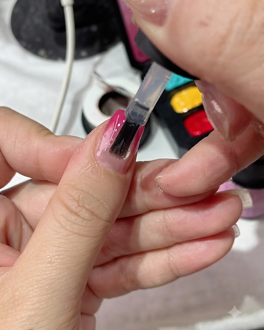 Un pincel de esmalte aplicando una capa superior transparente de manera uniforme sobre una uña con manicura degradada.