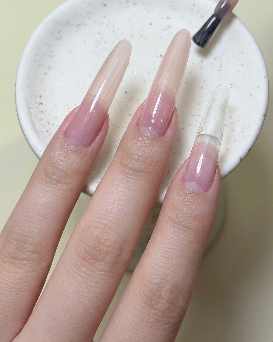 Pincel de uñas aplicando esmalte en gel rojo magenta en la uña del dedo índice.
