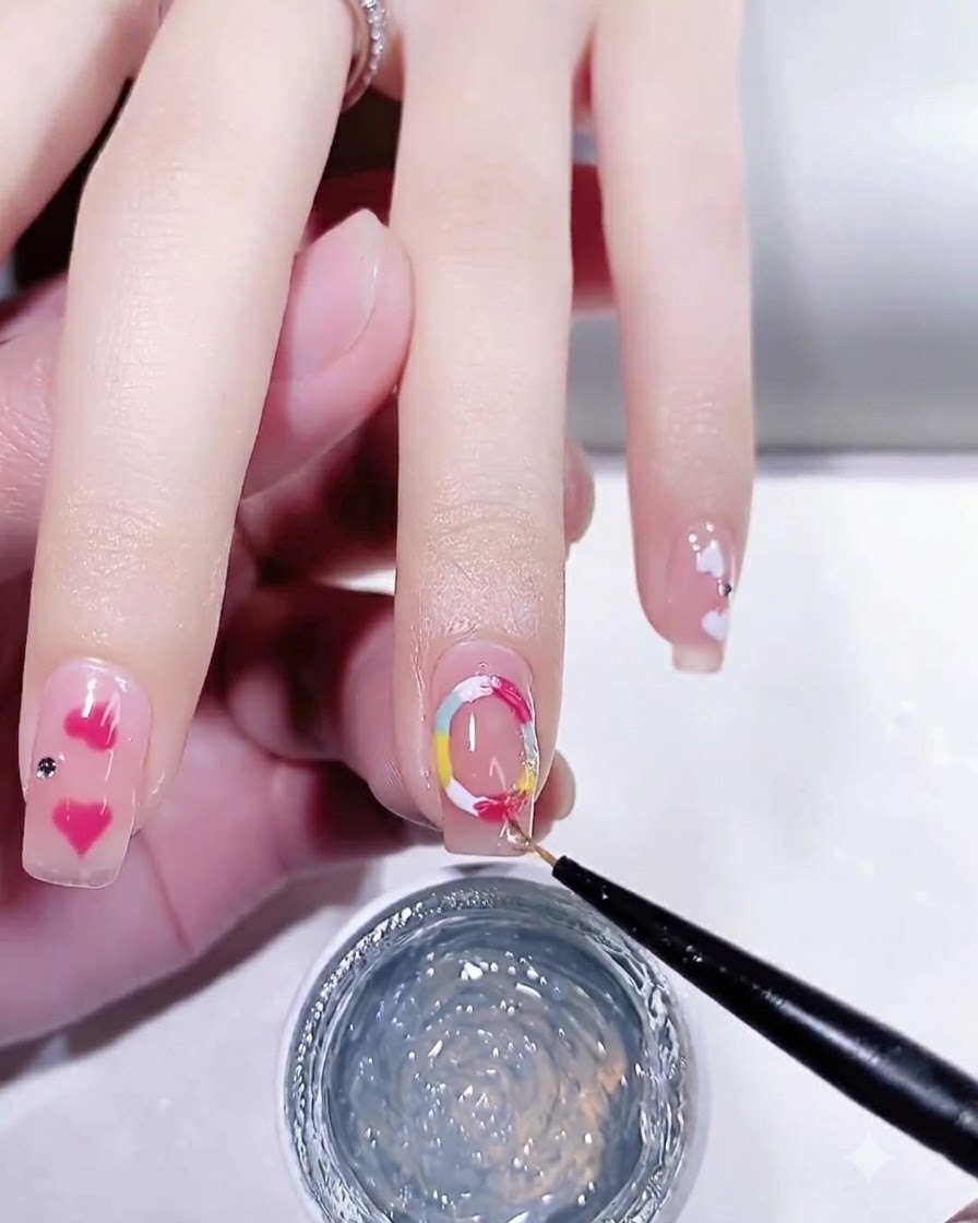 Un pincel de nail art aplicando un top coat brillante sobre una uña manicurada con detalles de puntos coloridos.