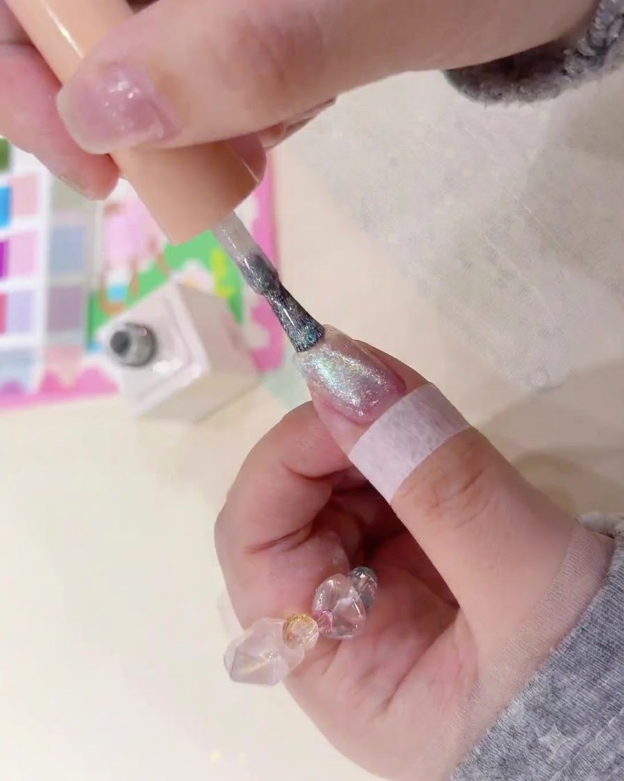 Una brocha aplicando gel ámbar magnético brillante sobre la superficie de una uña natural.