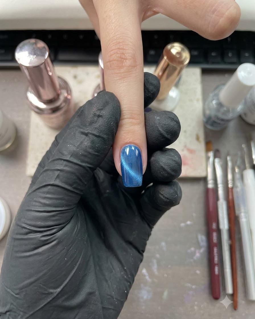 Un solo dedo con un acabado brillante en ojo de gato azul, posicionado en un entorno de estudio de uñas.